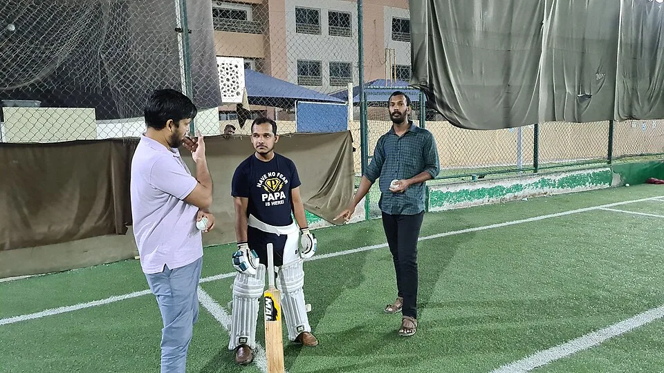 A batter discussing training with other cricketers beside the nets. CC0 sample; not Tailor academy photography.
